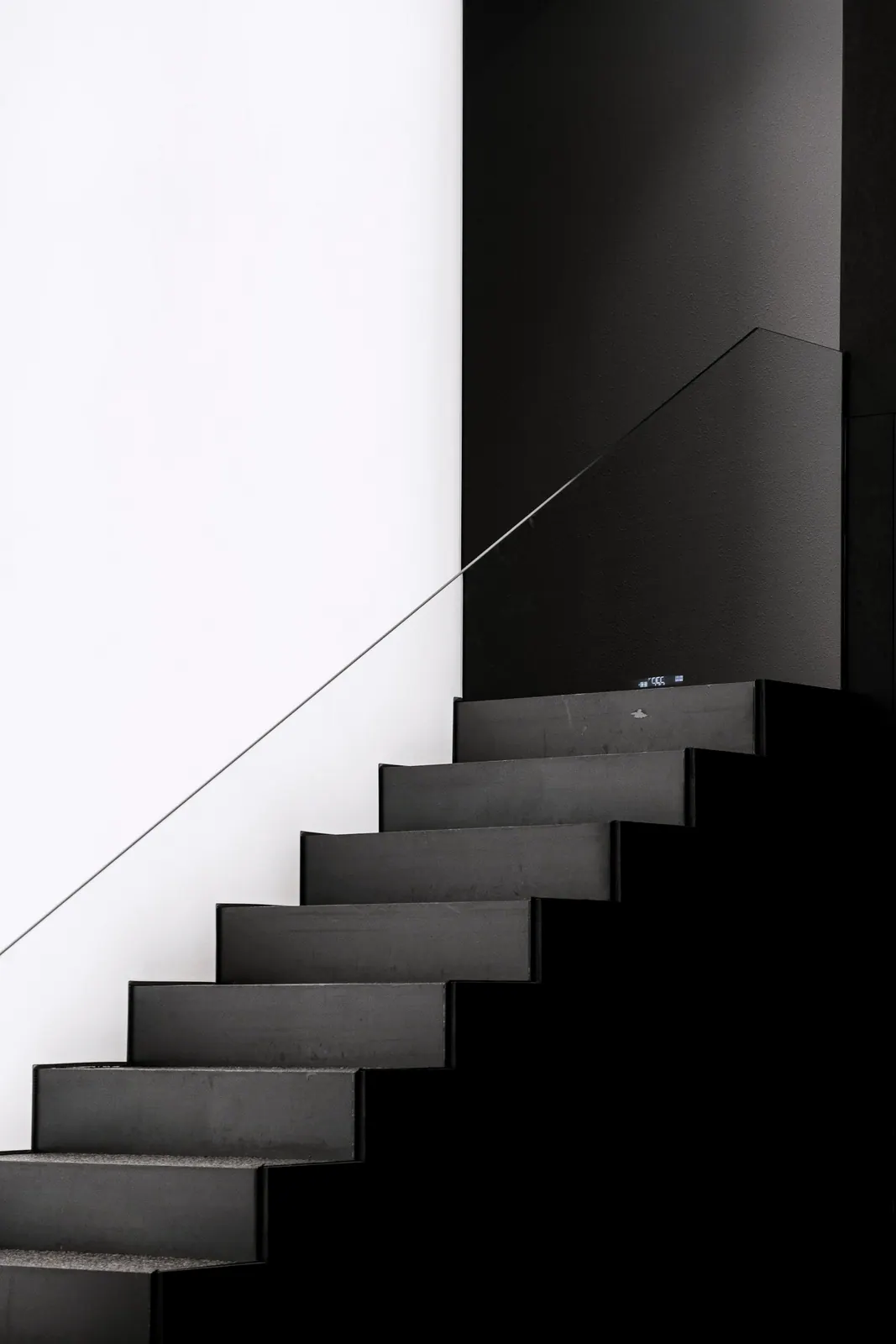 Volée d'escalier droite en acier sombre devant un mur clair, marches nettes et ombre portée verticale
