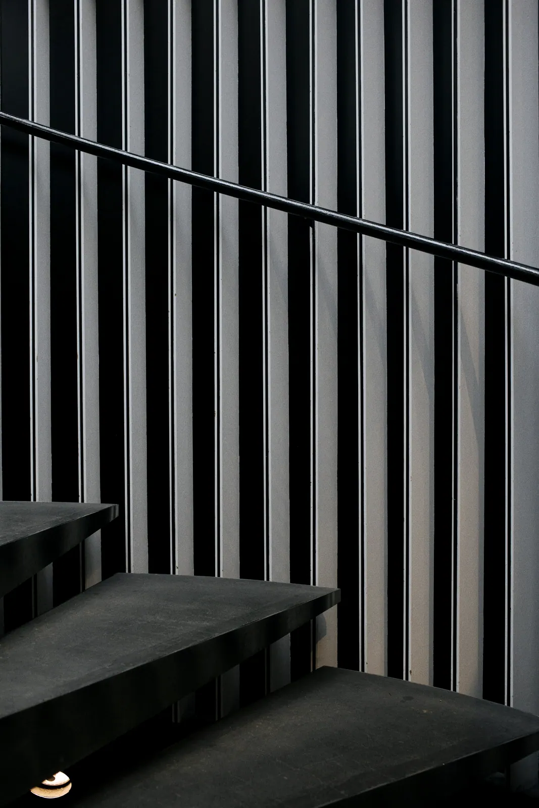 Escalier en acier sombre bordé d'un garde-corps à barreaudage vertical fin, en contre-jour