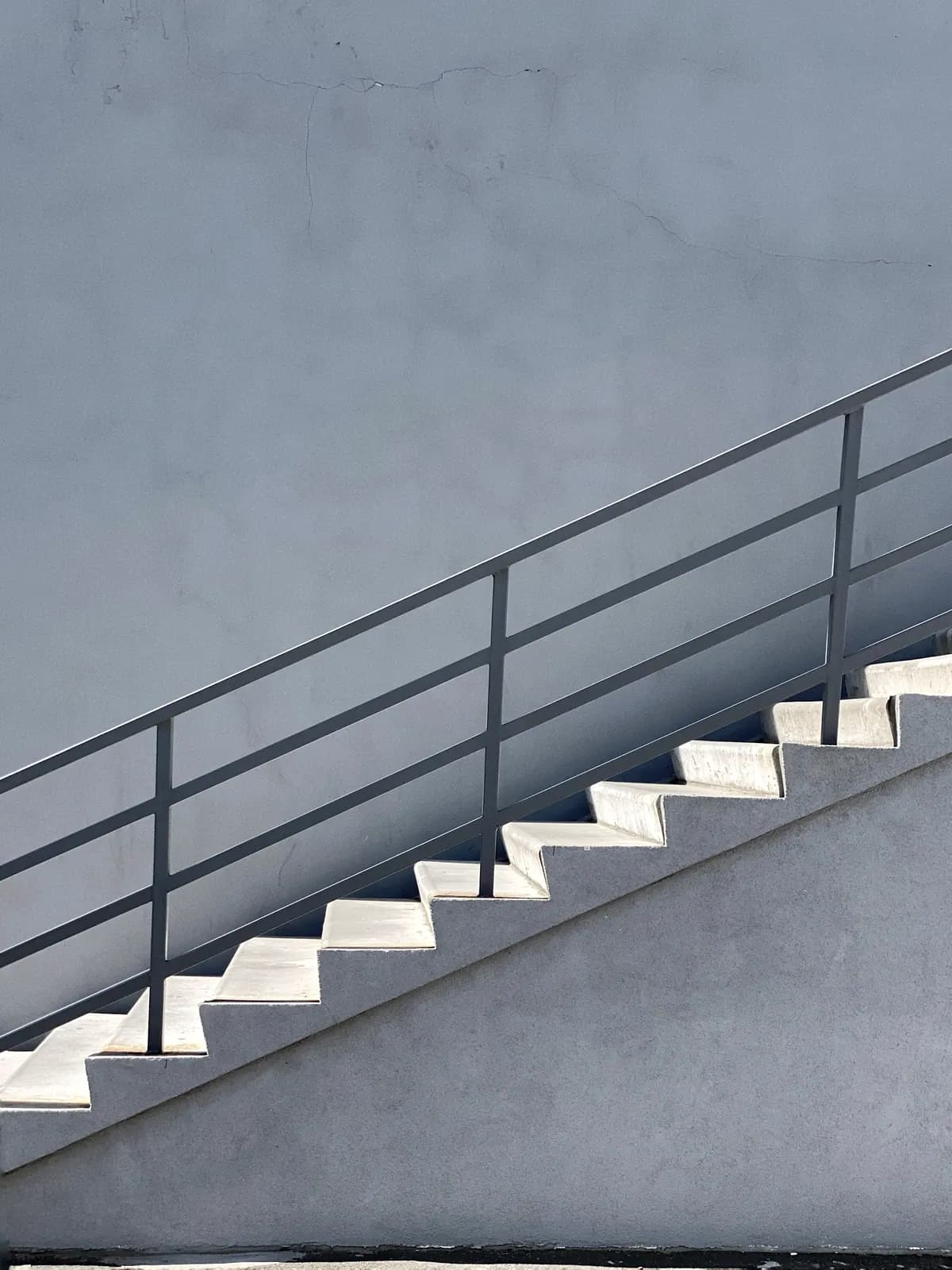 Main courante et garde-corps en acier sur un escalier, ombre portée dure sur le mur