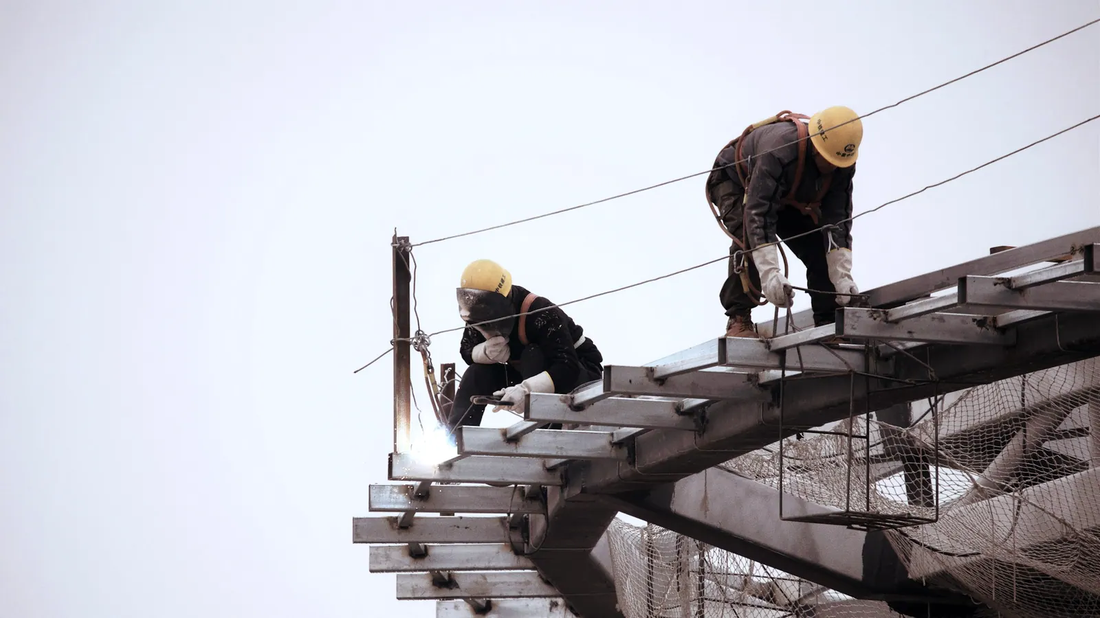 Pose d'une structure métallique sur un chantier, silhouettes casquées à distance